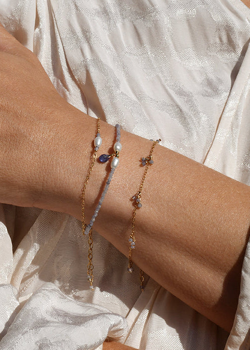 Close-up of a person's wrist with multiple tanzanite and keshi pearl bracelets on a light background