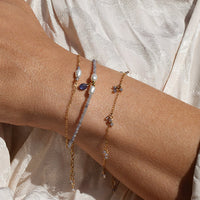 Close-up of a person's wrist with multiple tanzanite and keshi pearl bracelets on a light background