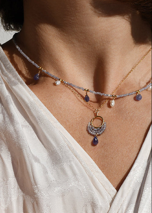 Close-up of a person wearing multiple necklaces and bracelets on a light background