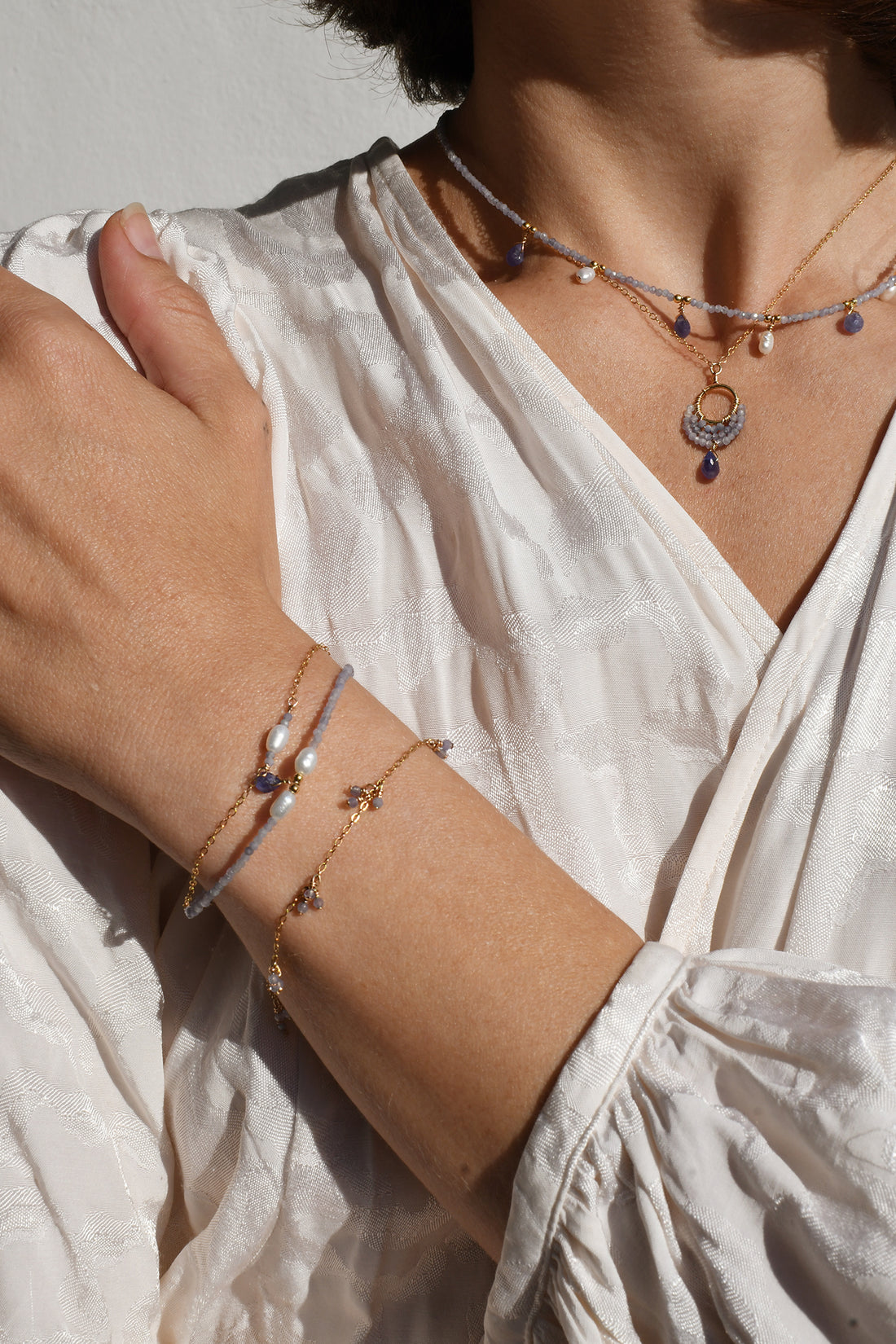 Close-up of a person wearing multiple necklaces and bracelets on a light background
