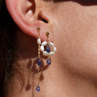 Close-up of a person wearing gold earrings with gemstones and keshi pearls against a neutral background