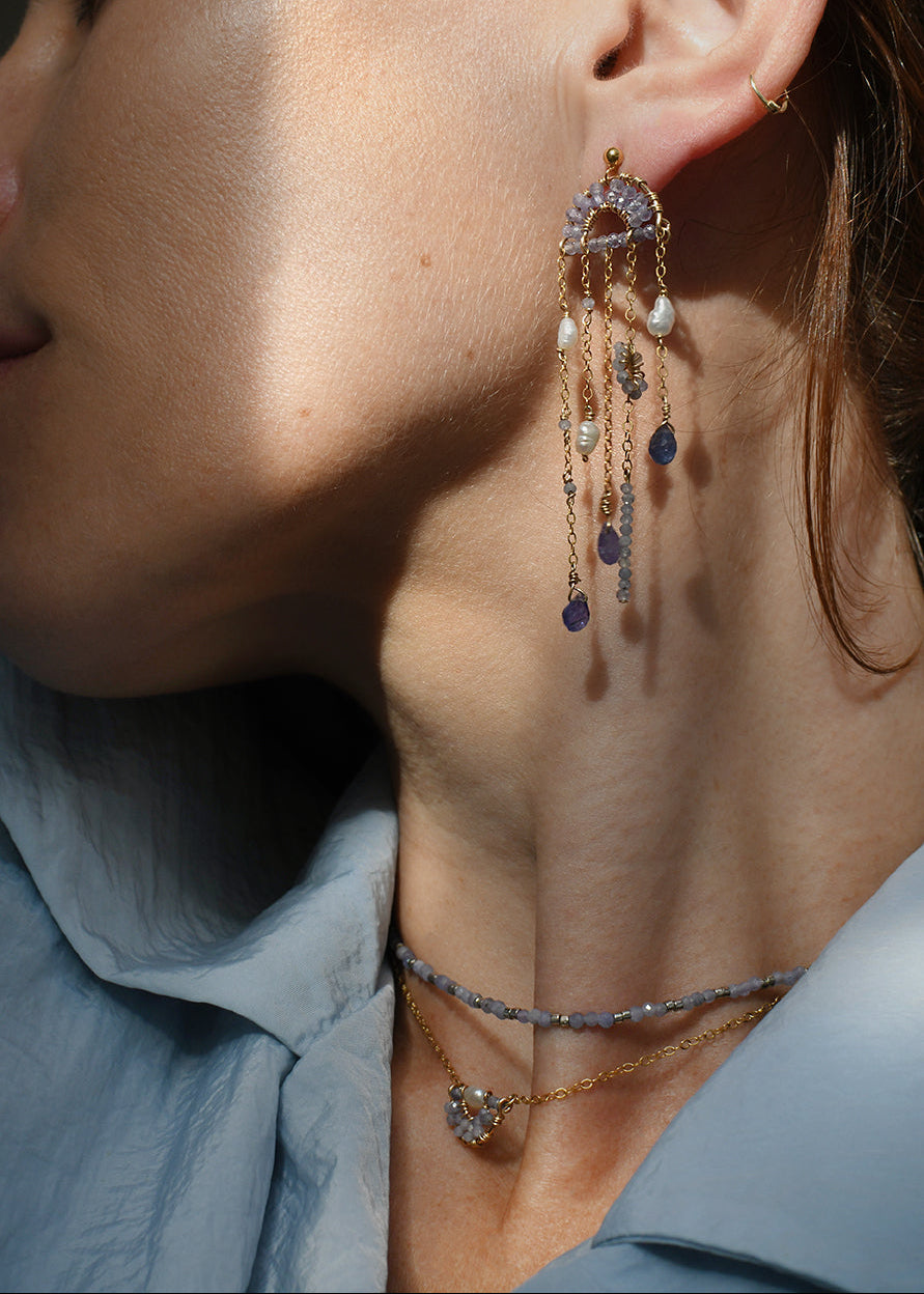 Close-up of a person wearing a dangling earring with pearls and gemstones.