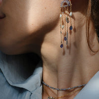 Close-up of a person wearing a dangling earring with pearls and gemstones.