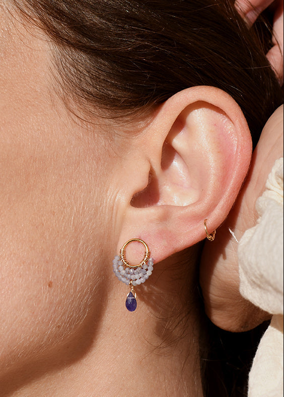 Close-up of a woman wearing gold stud  earrings with a blue purple tanzanite gemstone.