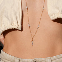 Necklace with a cross pendant on a person wearing a beige top and light-colored pants.