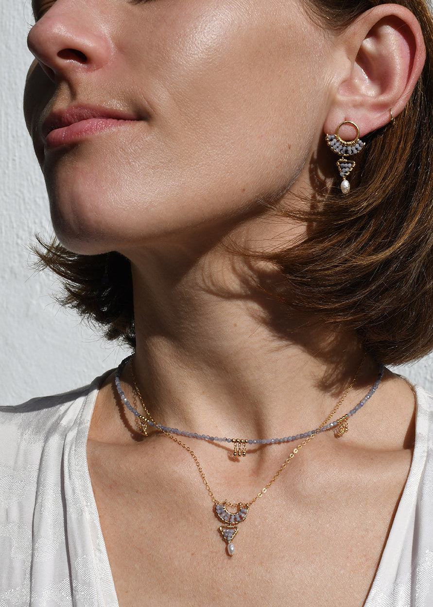 Close-up of a woman wearing gold tanzanite necklaces and earrings against a neutral background