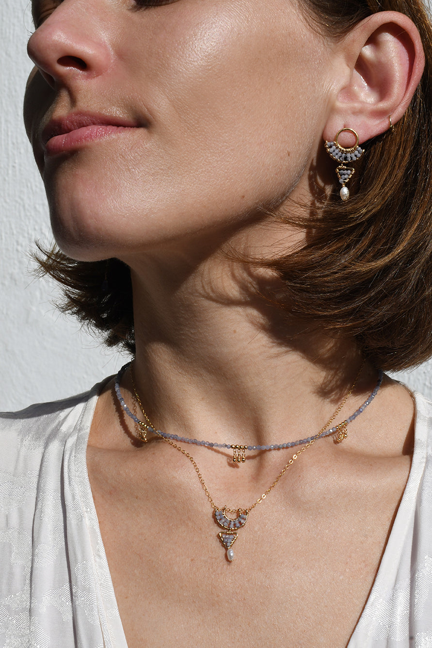 Close-up of a woman wearing gold necklaces and earrings against a neutral background