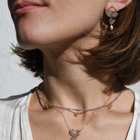 Close-up of a woman wearing gold necklaces and earrings against a neutral background