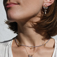 Close-up of a woman wearing gold tanzanite necklaces and earrings against a neutral background