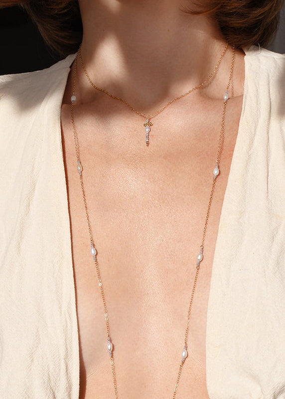 Person wearing a beige top with a necklace, standing outdoors.