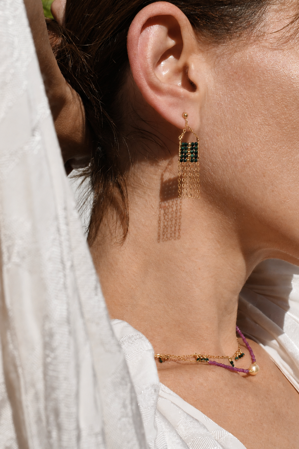 Close-up of a person wearing gold earrings with green gemstones and a matching bracelet.