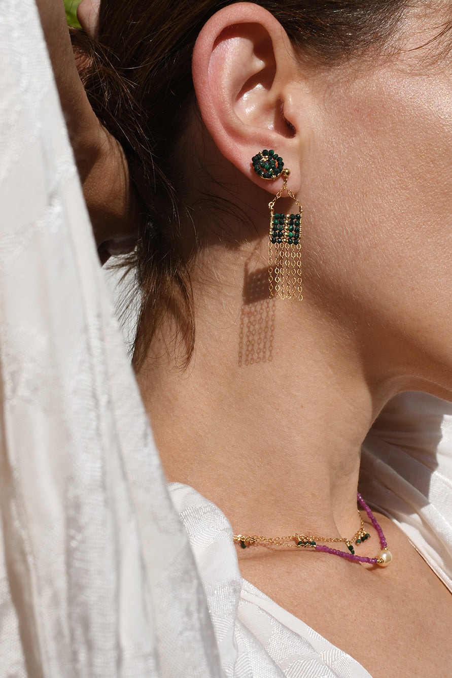 Close-up of a person wearing gold earrings with green gemstones and a matching bracelet.