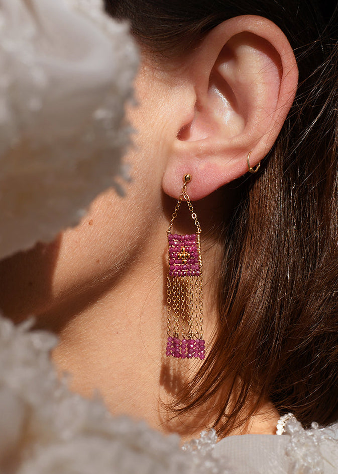 Close-up of an ear wearing a pink and gold earring with a soft, blurred background.