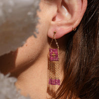 Close-up of an ear wearing a pink and gold earring with a soft, blurred background.