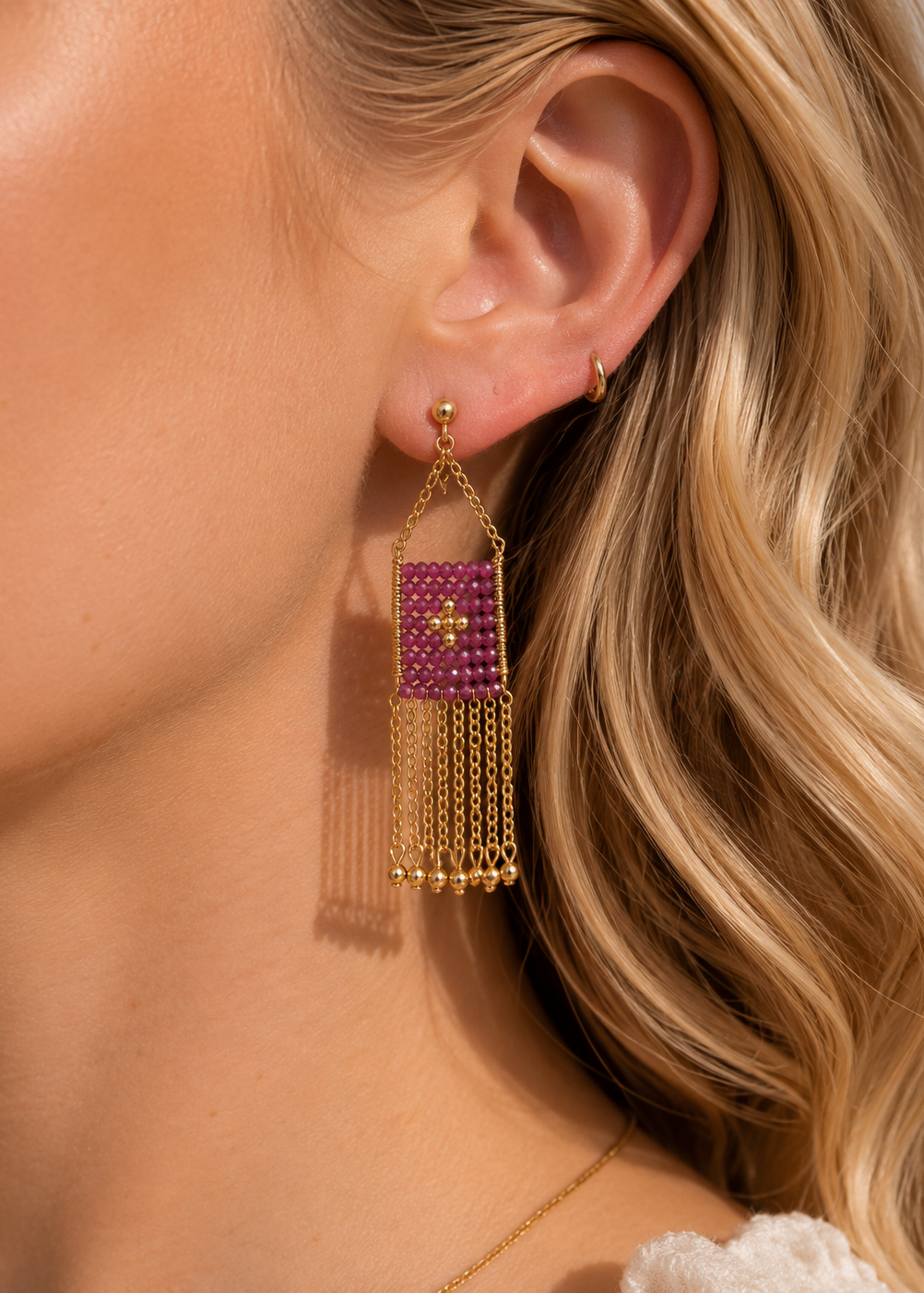 Close-up of a woman wearing a gold earring with a pink gemstone and dangling chains.