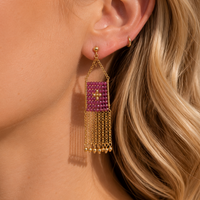 Close-up of a woman wearing a gold earring with a pink gemstone and dangling chains.