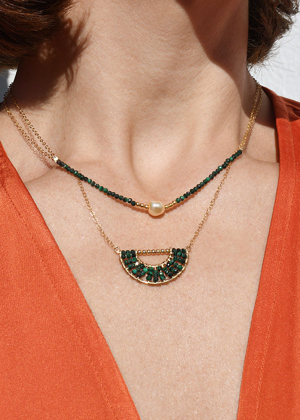 Close-up of a person wearing an orange top with a necklace and earrings.