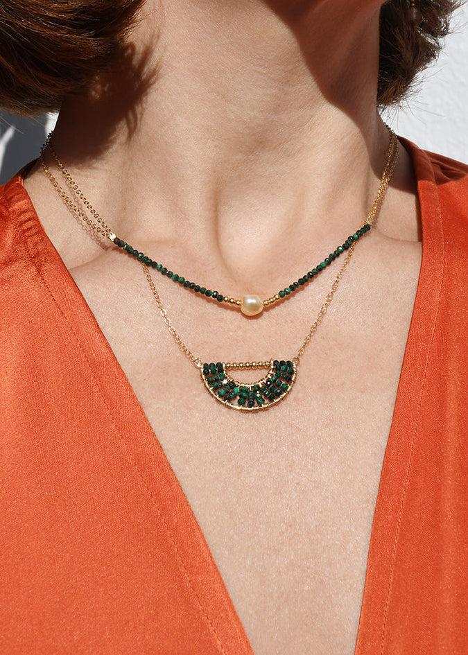 Close-up of a person wearing an orange top with a necklace and earrings.