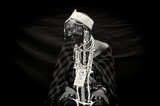 Portrait of Maasai lady wearing traditional check cloth (shuka), adorned with an elaborate head piece with hanging silver discs on chain, beaded mobile phone case and layered handmade beaded necklaces.  