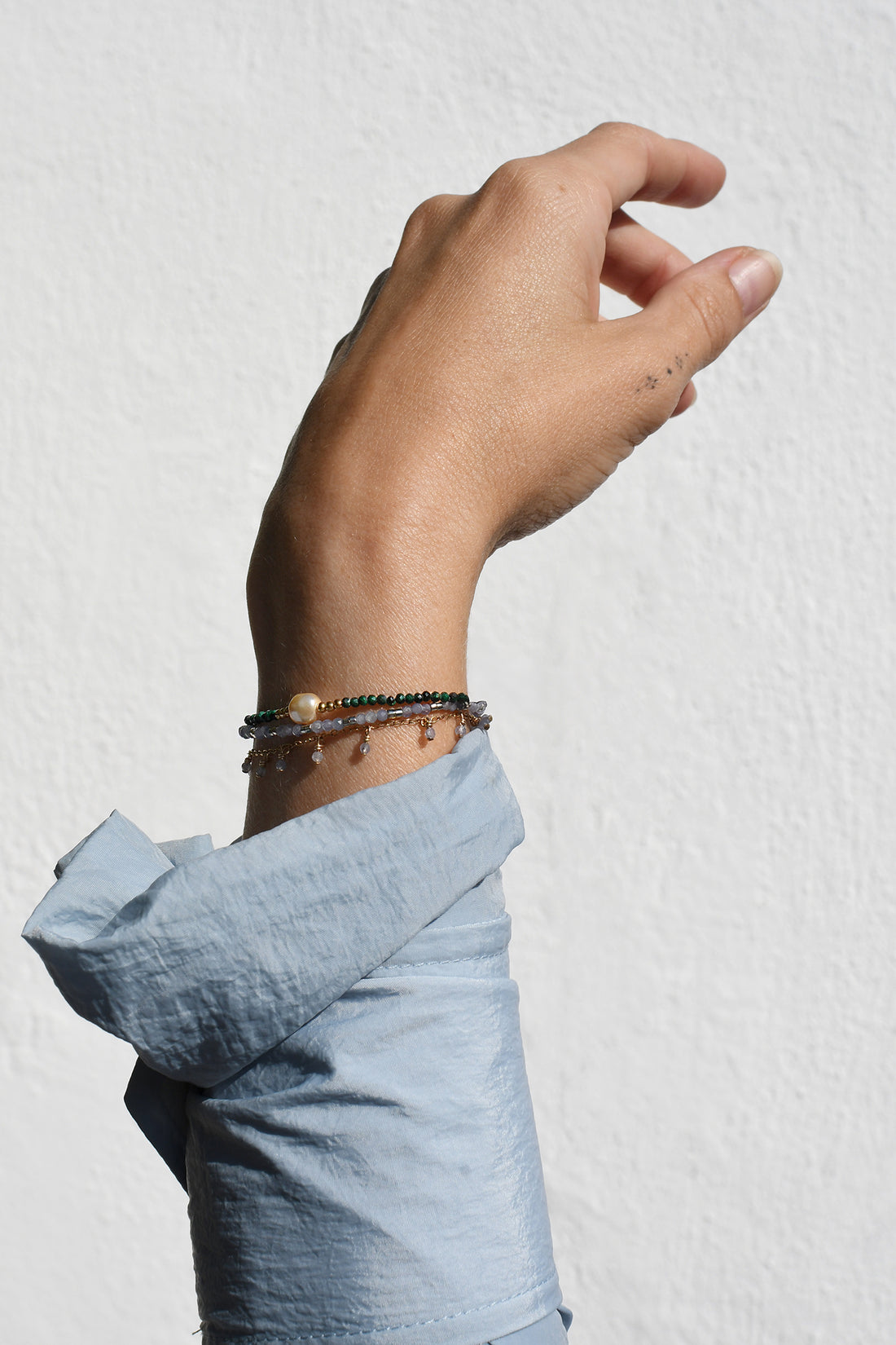Hand wearing multiple bracelets on a light gray background