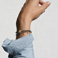 Hand wearing multiple bracelets on a light gray background