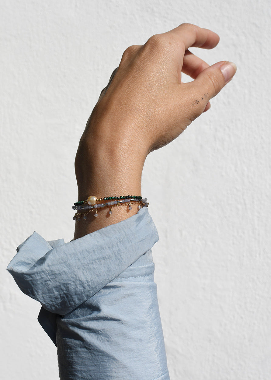 Hand wearing multiple bracelets on a light gray background