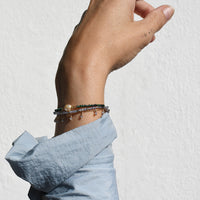 Hand wearing multiple bracelets on a light gray background