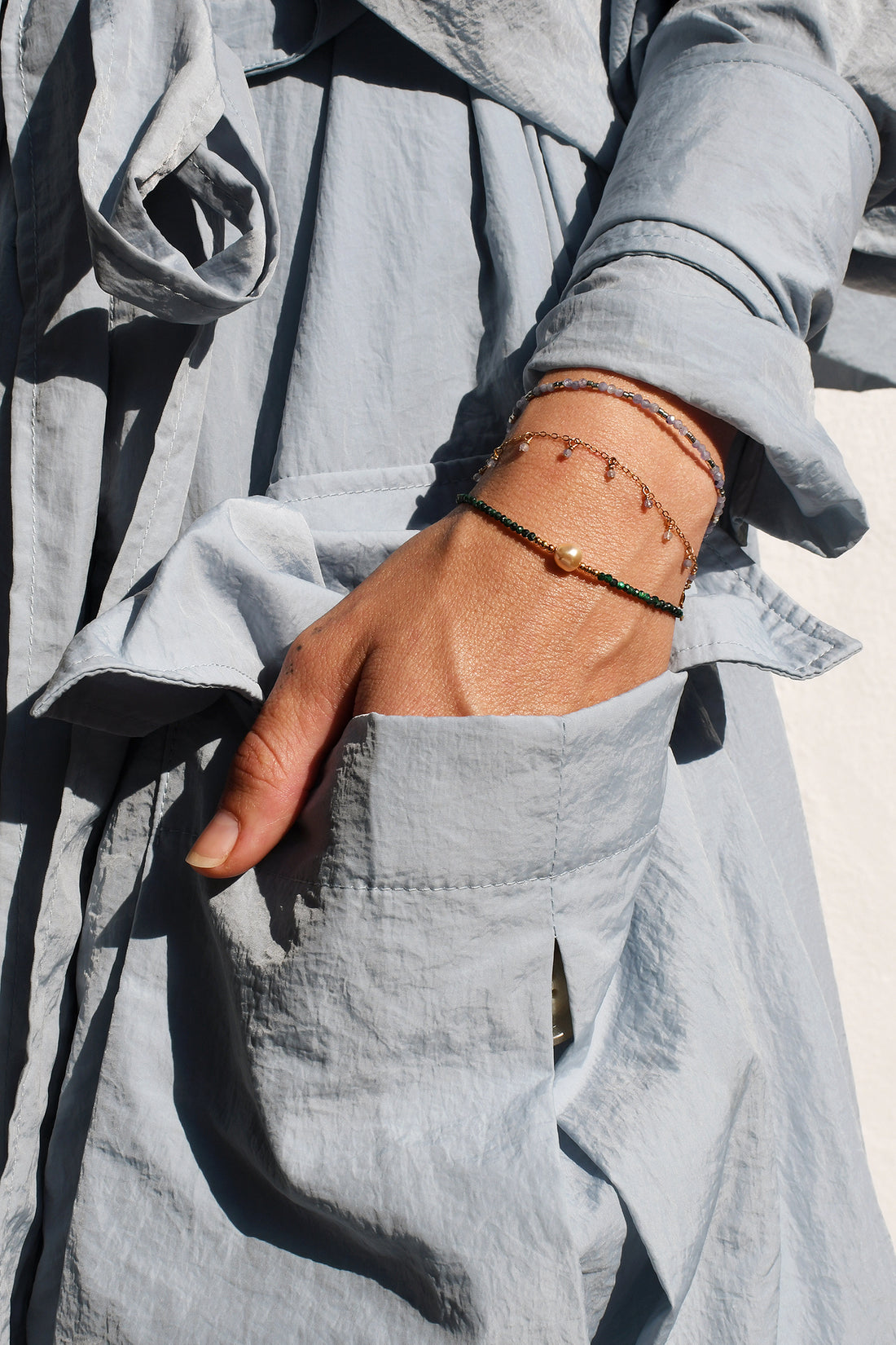 Person wearing a light gray outfit with a bracelet stack on a neutral background
