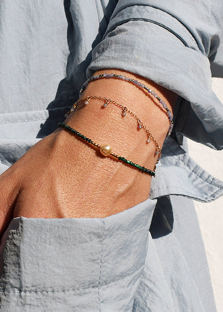 Person wearing a light gray outfit with a bracelet on a neutral background