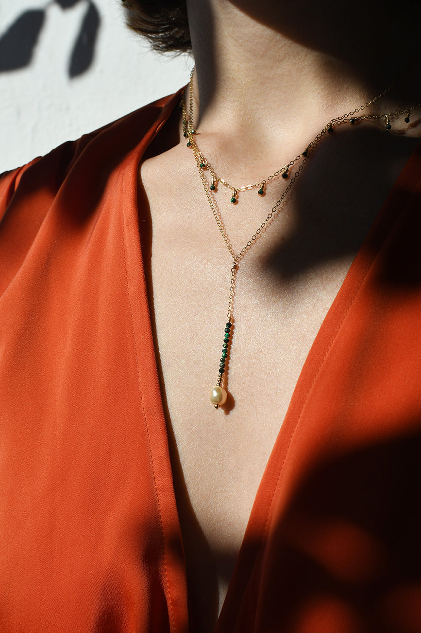 Close-up of a person wearing a gold necklace with green beads against a red garment.