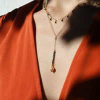 Close-up of a person wearing a gold necklace with green beads against a red garment.