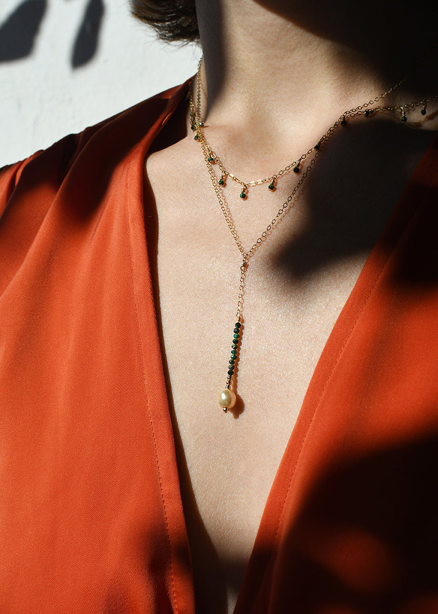 Close-up of a person wearing a gold necklace with green beads against a red garment.