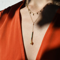 Close-up of a person wearing a gold necklace with green beads against a red garment.