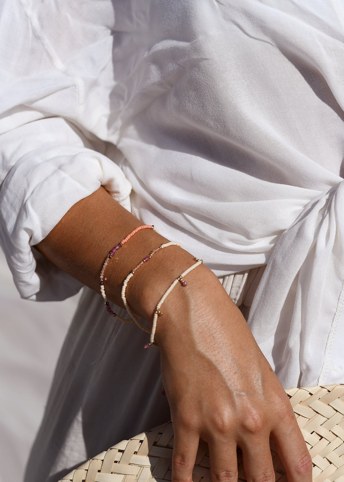 Close-up of a hand wearing multiple thin bracelets on a blurred white fabric background