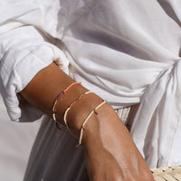 Close-up of a hand wearing multiple thin bracelets on a blurred white fabric background