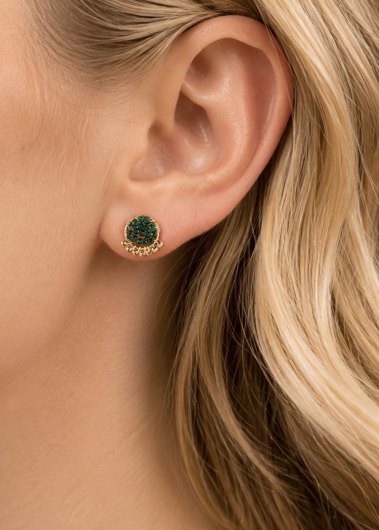 Close-up of a woman's ear wearing green gemstone earrings with gold settings.