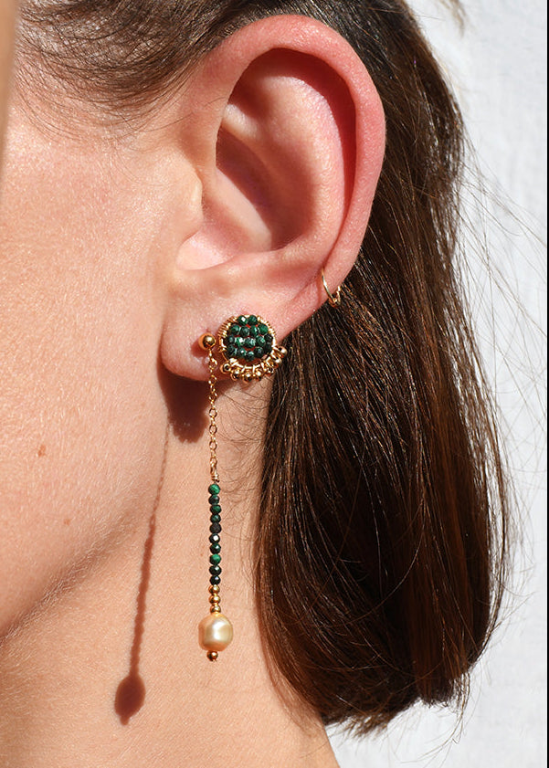 Close-up of a person wearing a green gemstone earring with dangling elements.