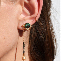 Close-up of a person wearing a green gemstone earring with dangling elements.