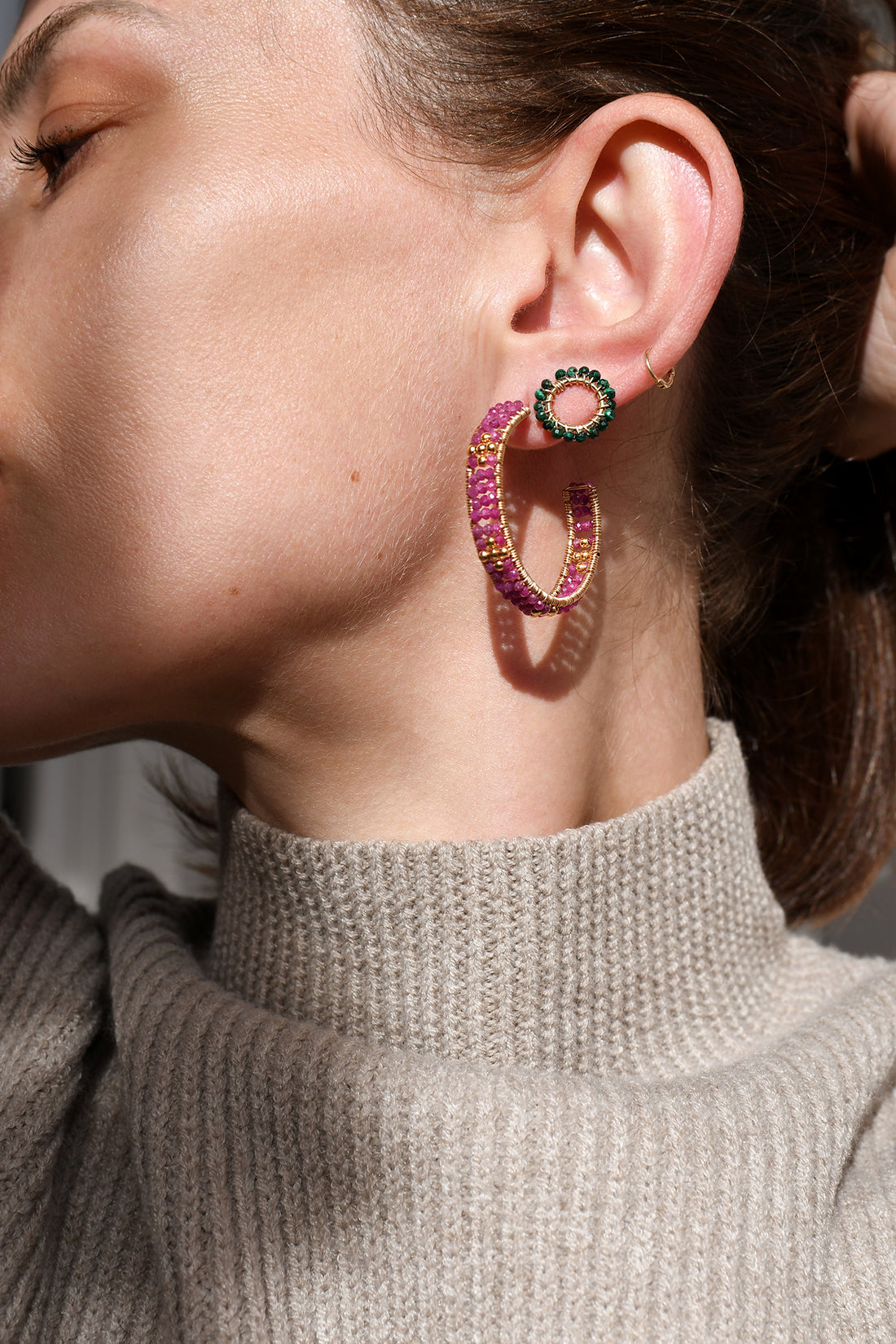 Close-up of a person wearing colorful hoop earrings with a neutral background