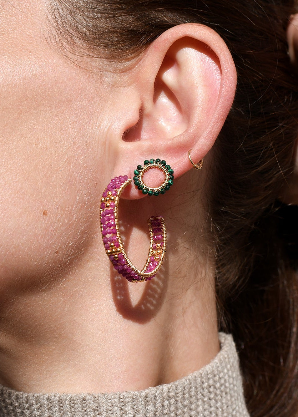Close-up of a person wearing colorful hoop earrings with a neutral background