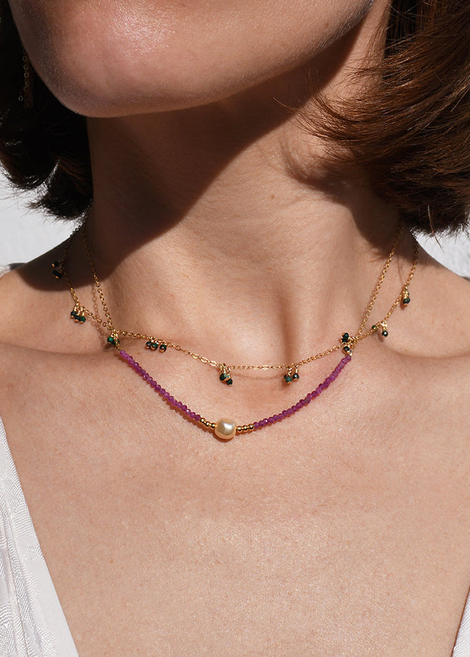 Close-up of a person wearing a necklace and earrings with a neutral background