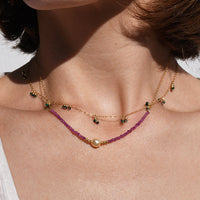 Close-up of a person wearing a necklace and earrings with a neutral background