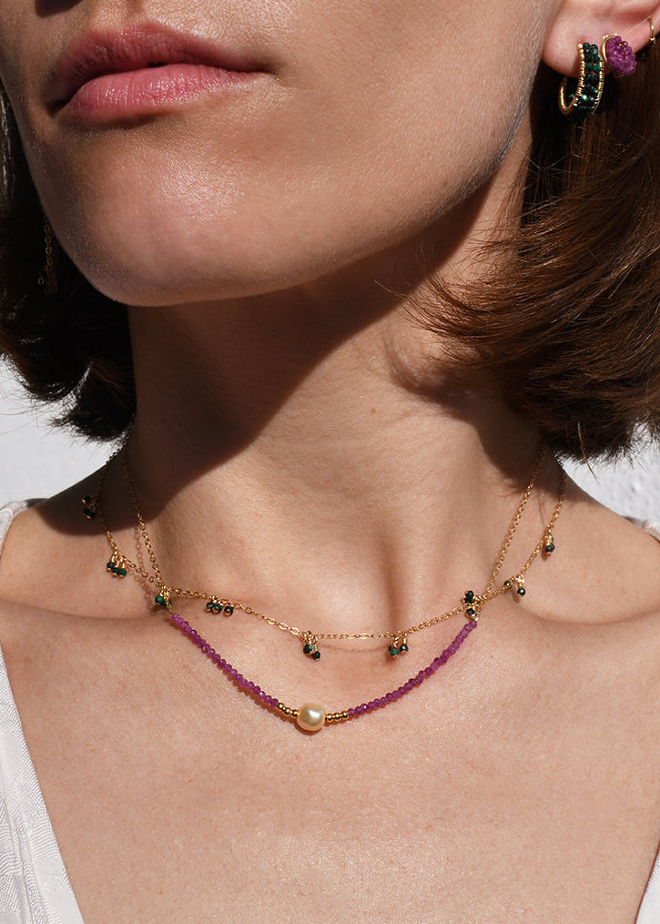 Close-up of a person wearing a necklace and earrings with a neutral background