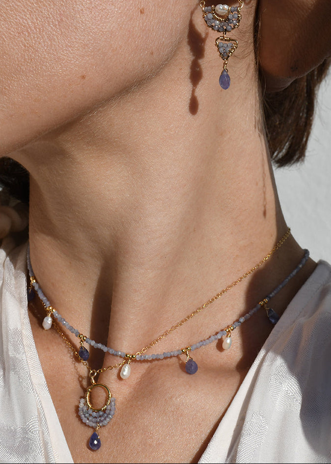 Close-up of a person wearing a necklace and earrings with a neutral background