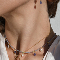 Close-up of a person wearing a necklace and earrings with a neutral background