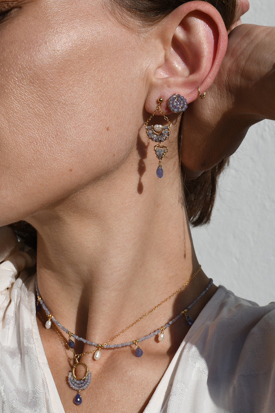 Close-up of a person wearing a necklace and tanzanite earrings with a neutral background
