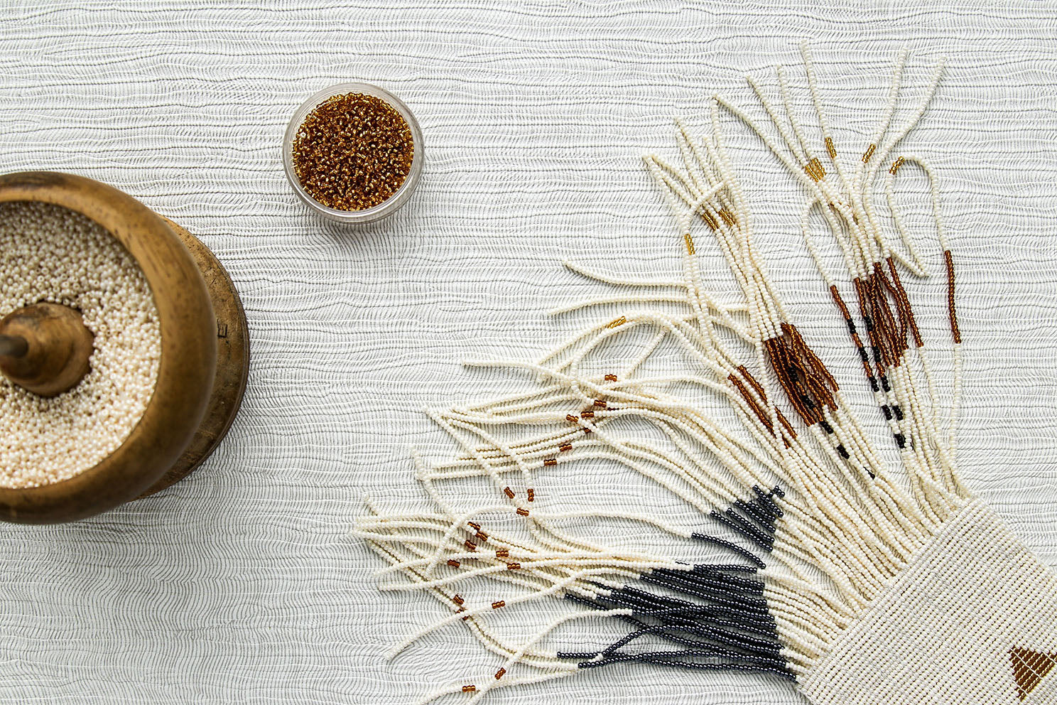 Modern hand beaded neutral colour wall hanging in pearl, graphite and tan. Positioned next to raw materials showing it in the making.