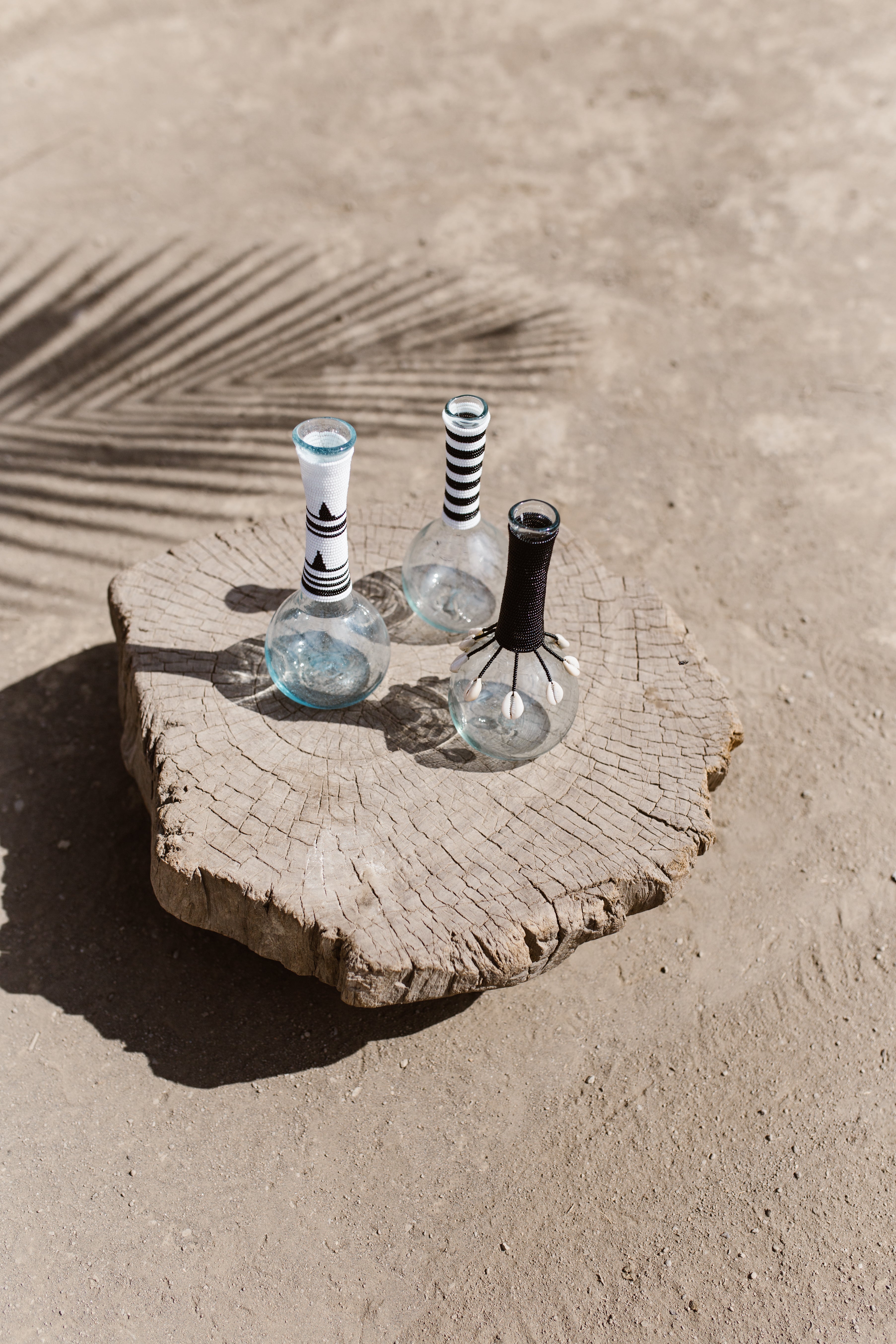 Modern monochromatic hand beaded decorative glass vases with stripes, triangles and solid black and shells on wood. 
